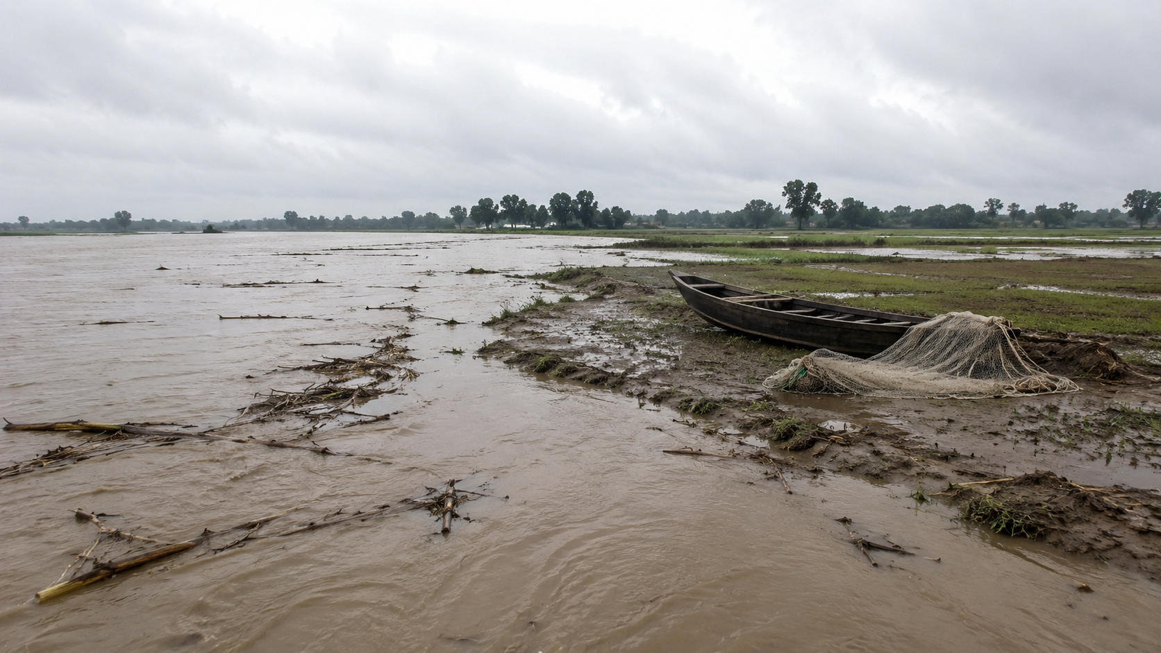Muddy floodwater covering farmland in north Bihar, with a fishing boat and unused net on the bank.
